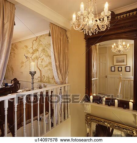 Stock Photo - Glass chandelier above staircase and landing with cream silk curtains on bannisters in front of small dining room. Fotosearch