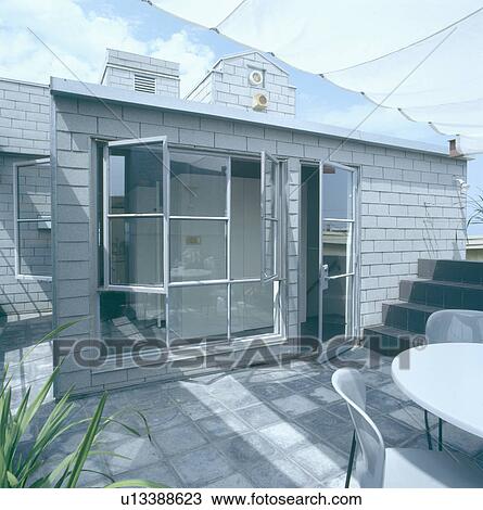Glass doors and windows leading on to city roof terrace with grey paving and table with chairs View Large Photo Image Stock Image - Glass doors and windows leading on to city roof terrace with grey paving and table with chairs. Fotosearch