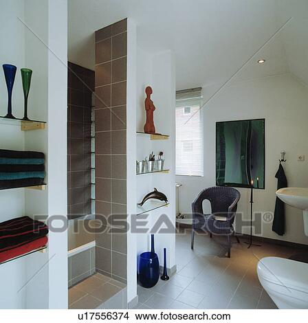 Picture - Glass shelves in alcoves in modern white bathroom with black wickere chair and grey floor tiles. Fotosearch