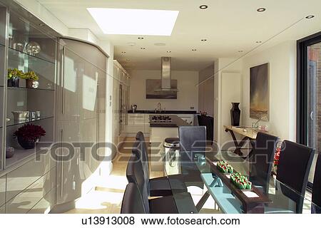 Stock Photo - Glass table and upholstered black chairs in modern openplan white kitchen. Fotosearch