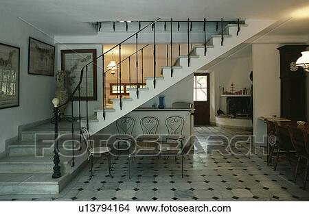 Picture - Grey and black tiled floor and stone staircase with iron bannisters in large openplan hall. Fotosearch