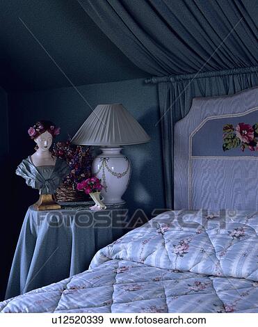 Stock Photo - Grey-blue ruched curtain on pole behind bed with blue+white striped and floral quilt in bedroom with bust and lamp on table. Fotosearch