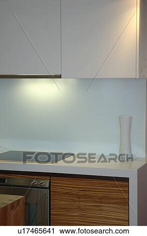 Stock Image - Grey cupboards above halogen hob in pastel blue modern kitchen. Fotosearch