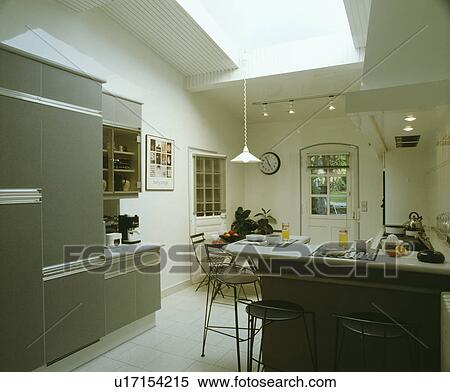 Stock Photography - Grey fitted cupboards in modern white kitchen with stools at breakfast bar. Fotosearch