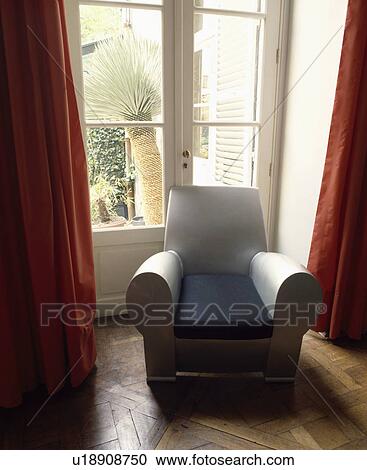 Stock Image - Grey plastic armchair in front of French doors. Fotosearch