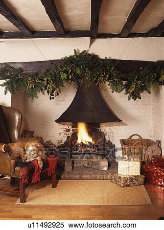 Stock Photography - Holy+ivy Christmas garland above lighted fire in beamed traditional living room. Fotosearch