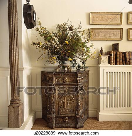 Informal flower arrangement on antique carved wooden cupboard in cream hall with pictures and books above radiator cover View Large Photo Image Stock Photo - Informal flower arrangement on antique carved wooden cupboard in cream hall with pictures and books above radiator cover. Fotosearch