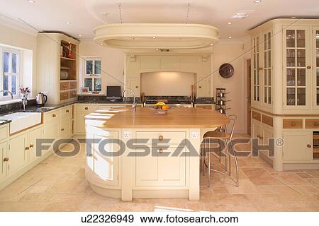 Stock Photo - Island unit with stools at breakfast bar in modern cream kitchen with limestone floor tiles. Fotosearch