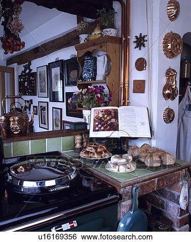 Stock Photograph - Large mirror above black Aga beside scones and bread rolls on worktop with cookery book on stand. Fotosearch