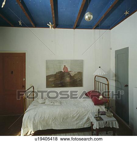Large picture above single brass bed with white bed-cover in small white bedroom with lighted lamp above bed View Large Photo Image Stock Photo - Large picture above single brass bed with white bed-cover in small white bedroom with lighted lamp above bed. Fotosearch
