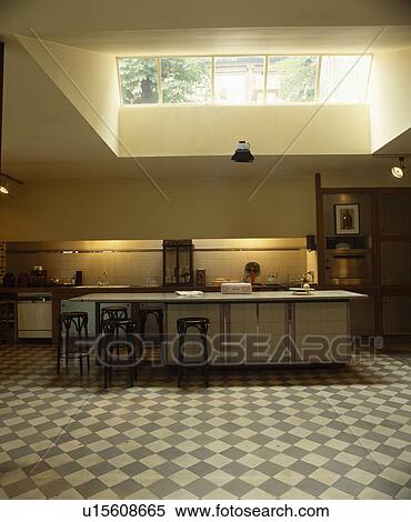 Stock Photography - Large skylight above modern kitchen extension with breakfast bar and grey+white chequerboard floor. Fotosearch