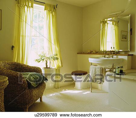 Stock Photo - Large traditional white bathroom with wicker chair and sheer curtains . Fotosearch