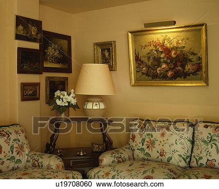 Stock Image - Lighted picture on wall above floral sofa in traditional living room. Fotosearch