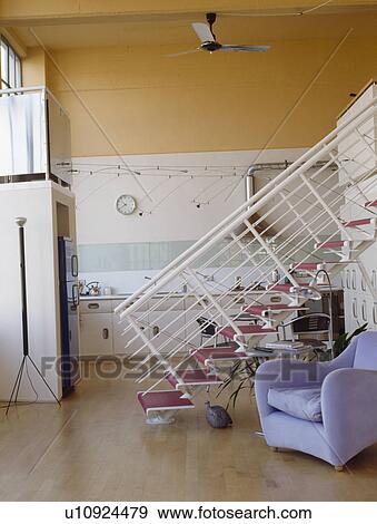 Stock Photo - Lilac Matthew Hilton 'Balzac' chair in front of metal staircase in openplan loft conversion kitchen and living area. Fotosearch