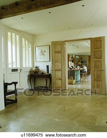 Stock Photography - Limestone floor tiles in cream hall with open double wooden doors and view of mother and daughter in kitchen. Fotosearch