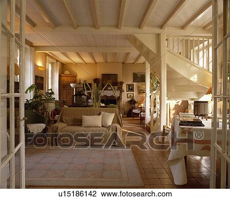 Stock Image - Loosecover on sofa in traditional openplan living room with cream beamed ceiling. Fotosearch