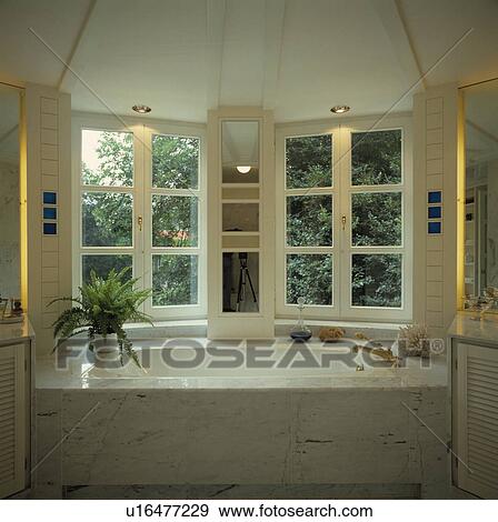 Marble surround on white bath below casement windows in white bathroom View Large Photo Image Stock Photo - Marble surround on white bath below casement windows in white bathroom. Fotosearch