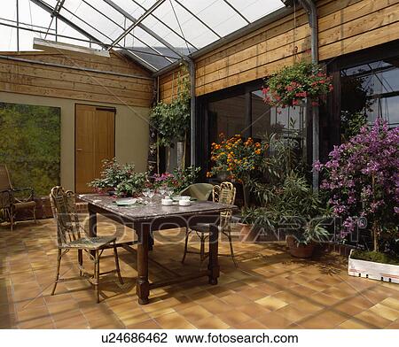Stock Image - Marble topped table and cane chairs in conservatory dining room with tiled floor. Fotosearch