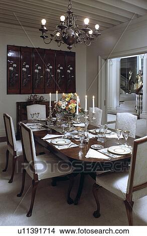 Picture - Metal chandelier above antique table and white upholstered chairs in white dining room. Fotosearch