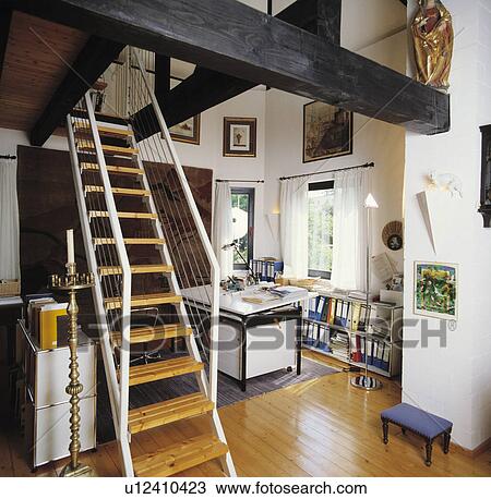 Stock Image - Metal staircase with open wooden treads in modern hall study with wooden flooring and black beams. Fotosearch