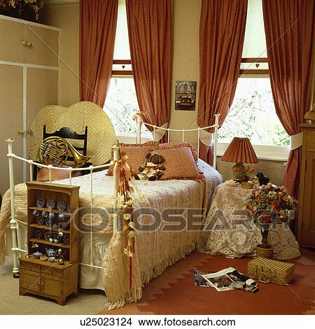 Miniature dresser below single white iron bed in child's bedroom with terracotta curtains and rug View Large Photo Image Picture - Miniature dresser below single white iron bed in child's bedroom with terracotta curtains and rug. Fotosearch