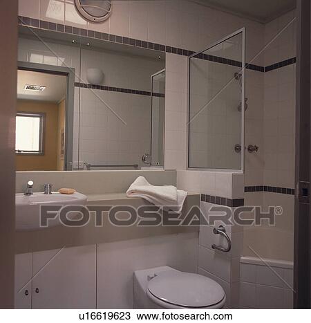 Mirror above fitted basin and toilet beside shower and bath in modern white bathroom View Large Photo Image Stock Image - Mirror above fitted basin and toilet beside shower and bath in modern white bathroom. Fotosearch