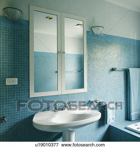Mirrored cabinet inset in blue mosaic wall above white pedestal basin in modern bathroom View Large Photo Image Stock Photo - Mirrored cabinet inset in blue mosaic wall above white pedestal basin in modern bathroom. Fotosearch