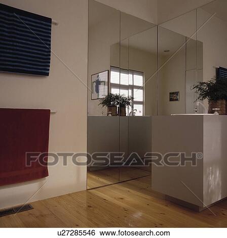 Mirrored wall in modern white bathroom with wooden flooring View Large Photo Image Stock Photograph - Mirrored wall in modern white bathroom with wooden flooring. Fotosearch