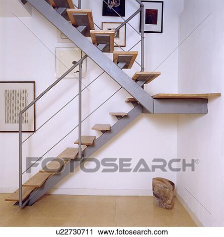 Stock Image - Modern metal staircase with wooden treads in white hall with wooden flooring. Fotosearch