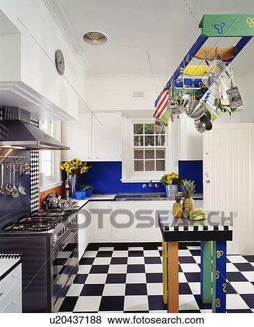 Multicoloured rack above matching table in modern white kitchen with black range oven and black+white flooring View Large Photo Image Stock Photo - Multicoloured rack above matching table in modern white kitchen with black range oven and black+white flooring. Fotosearch