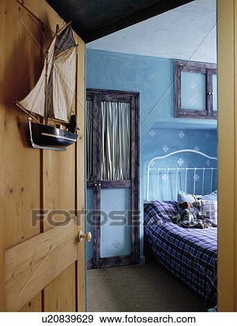 Stock Photo - Open pine door to child's blue bedroom with white iron bed and stamped paint effect walls. Fotosearch