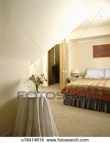 Stock Photograph - Orange+green patchwork quilt in white attic bedroom with cream carpet. Fotosearch