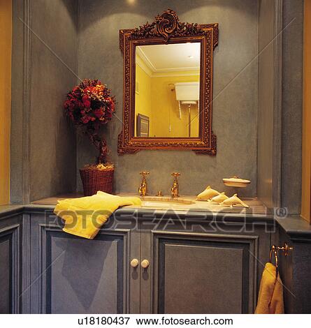 Ornate rectangular gilt mirror above basin in vanity unit with cream towel in grey cloakroom View Large Photo Image Stock Photo - Ornate rectangular gilt mirror above basin in vanity unit with cream towel in grey cloakroom. Fotosearch