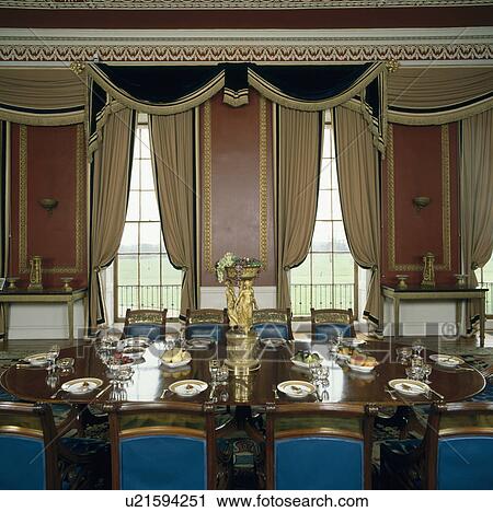 Ornate swagged curtains in large country house dining room with blue chairs and place settings on the table View Large Photo Image Stock Image - Ornate swagged curtains in large country house dining room with blue chairs and place settings on the table. Fotosearch
