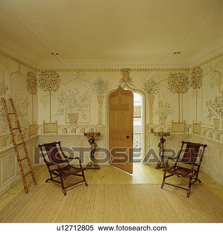 Stock Photography - Painted trompe l'oeil mural in small hall with antique campaign chairs and Gothic door. Fotosearch