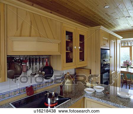 Pale wood fitted cupboards with utensil storage above lighted halogen hob in kitchen with wooden ceiling View Large Photo Image Stock Photo - Pale wood fitted cupboards with utensil storage above lighted halogen hob in kitchen with wooden ceiling. Fotosearch
