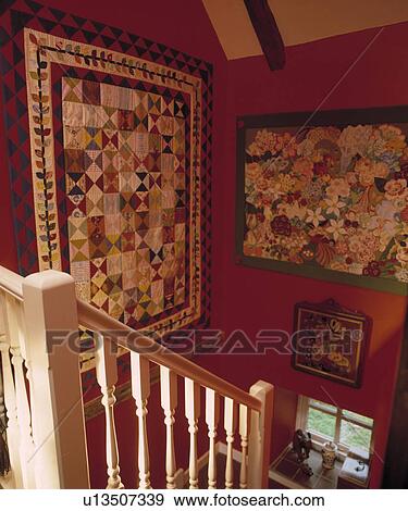 Patchwork quilts on red walls above wooden staircase in country hall View Large Photo Image Stock Photo - Patchwork quilts on red walls above wooden staircase in country hall. Fotosearch