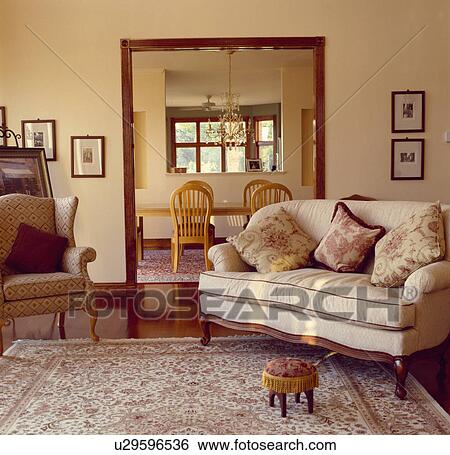 Patterned armchair and cream sofa with toile-de-Jouy cushions in front of doorway in livingroom with small footstool on patterned carpet View Large Photo Image Stock Photograph - Patterned armchair and cream sofa with toile-de-Jouy cushions in front of doorway in livingroom with small footstool on patterned carpet. Fotosearch