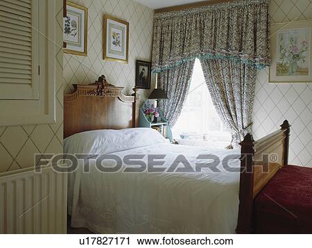 Patterned curtains with deep pelmet in small country bedroom with wallpaper and antique wooden bed View Large Photo Image Stock Image - Patterned curtains with deep pelmet in small country bedroom with wallpaper and antique wooden bed. Fotosearch
