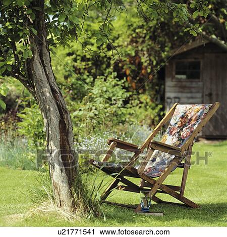 Stock Image - Patterned deckchair below tree on lawn in country garden in summer. Fotosearch
