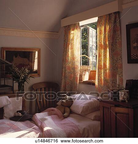 Stock Photograph - Patterned orange floral curtains at open window above single bed with pink pillow and patchwork quilt in child's bedroom. Fotosearch