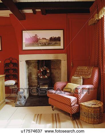 Patterned red armchair beside stove in fireplace in traditional red living room View Large Photo Image Stock Photo - Patterned red armchair beside stove in fireplace in traditional red living room. Fotosearch