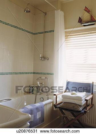 Stock Image - Pile of towels on director's chair in cream bathroom with tiled walls above bath and shower. Fotosearch