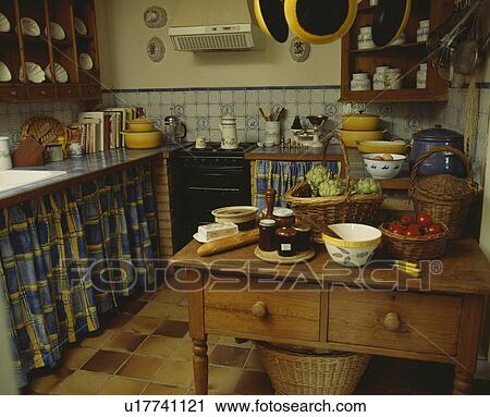 Stock Image - Pine table in old-fashioned cottage kitchen with blue curtains below worktops. Fotosearch