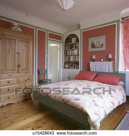 Stock Image - Pink pillows and floral duvet in pink bedroom with pine wardrobe. Fotosearch