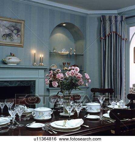 Pinks in glass vase on table with place settings in pale blue dining room with lighted shelving in alcove View Large Photo Image Stock Photograph - Pinks in glass vase on table with place settings in pale blue dining room with lighted shelving in alcove. Fotosearch