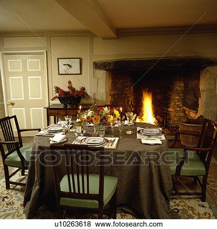 Place settings and floral arrangement on table with brown cloth in front of fireplace in country dining room View Large Photo Image Stock Photo - Place settings and floral arrangement on table with brown cloth in front of fireplace in country dining room. Fotosearch
