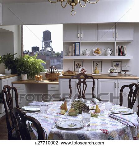 Place settings on patchwork cloth on circular table in white kitchen with view of city through window View Large Photo Image Stock Image - Place settings on patchwork cloth on circular table in white kitchen with view of city through window. Fotosearch