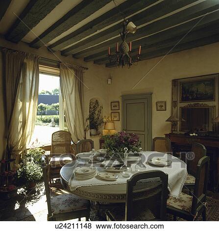Plates a on circular table with white cloth in beamed country dining room with French doors View Large Photo Image Stock Photo - Plates a on circular table with white cloth in beamed country dining room with French doors . Fotosearch