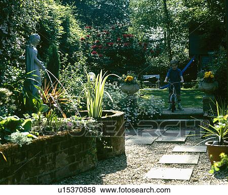 Raised bed and pond with fountain statue in town garden with paving slabs on gravel and small boy on bicycle View Large Photo Image Stock Photo - Raised bed and pond with fountain statue in town garden with paving slabs on gravel and small boy on bicycle. Fotosearch